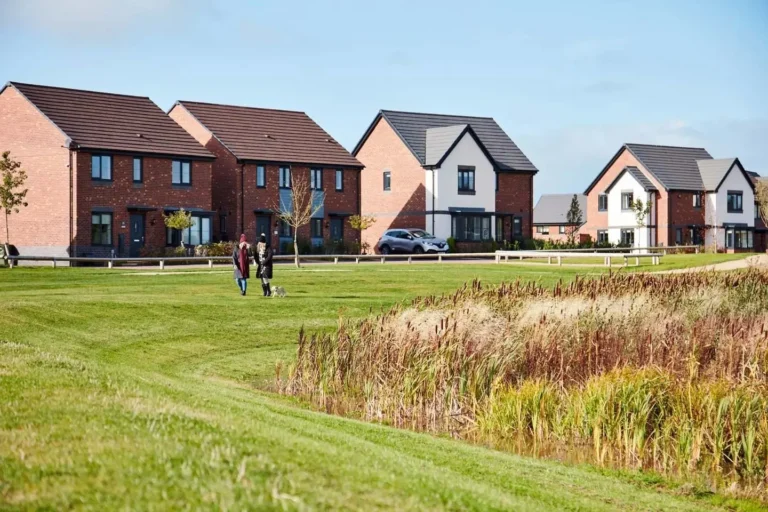 Two women are walking their dogs across green space in front of new houses on the Burleyfields development in Stafford.